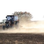 Rolnik jedzie czerwonym ciągnikiem po zapylonym polu przed siewem