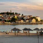 Zachód słońca nad plażą z parasolami i miasteczkiem Primošten w Chorwacji