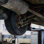 Mechanik ogląda od spodu zawieszenie samochodu na podnośniku w warsztacie
