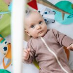 Niemowlę w śpioszkach bawi się na kolorowej macie w domu