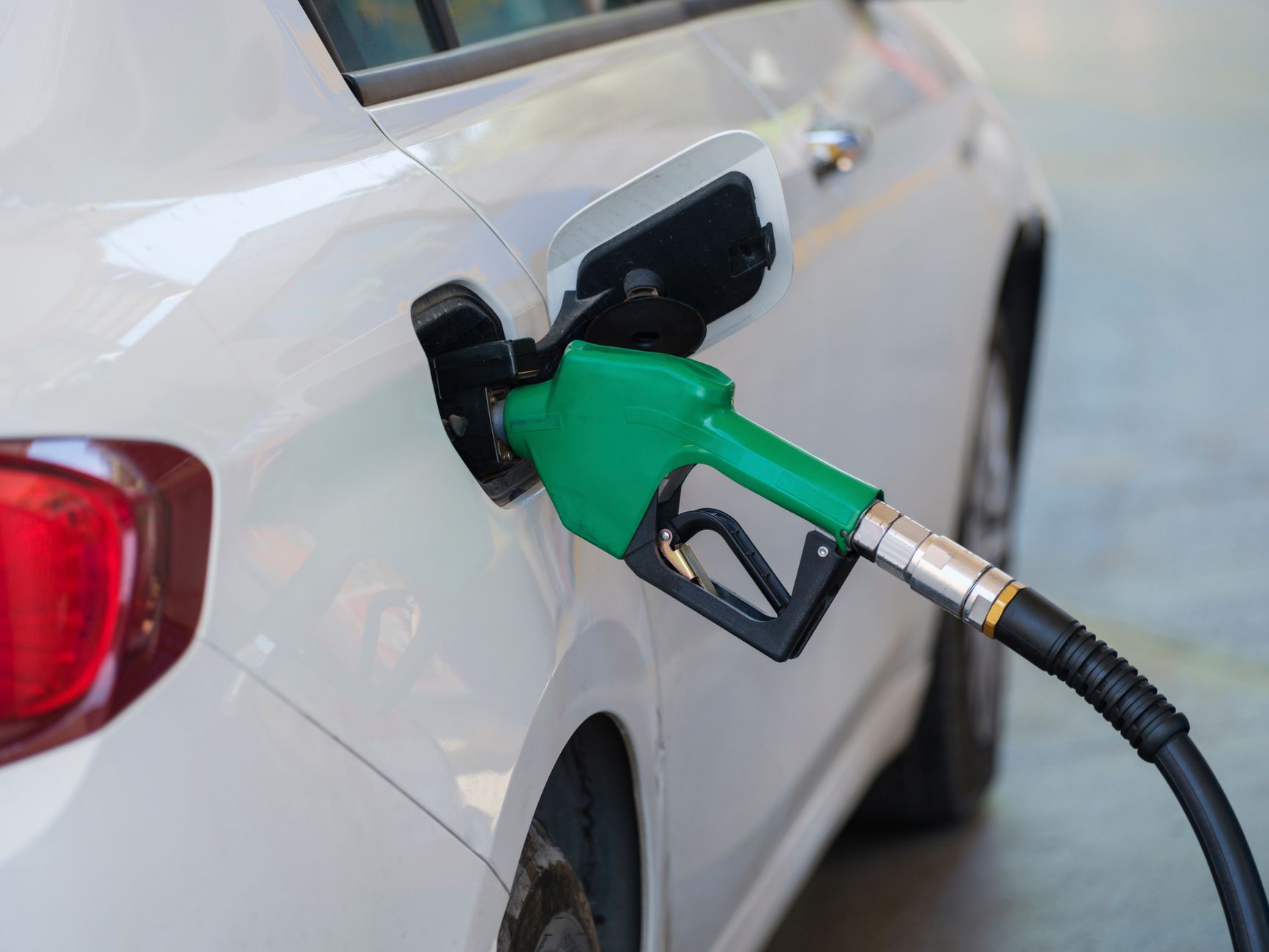 Zielony pistolet dystrybutora tankuje białe auto na stacji paliw Zielony pistolet dystrybutora tankuje białe auto na stacji paliw
